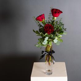 Red roses arranged in a clear glass vase with greenery