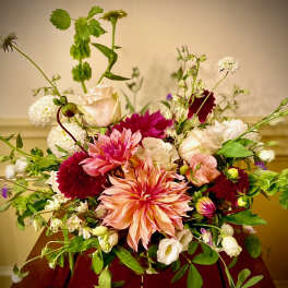 Airy arrangement of peach dahlias with pink and white roses in a low vase on a wooden table