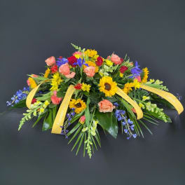 Colorful floral casket spray with roses, sunflowers, and blue accents