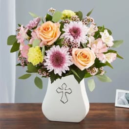 Pastel flower arrangement in a white vase with a cross emblem