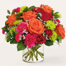 Mixed bouquet of orange, pink, and red flowers in a clear glass vase