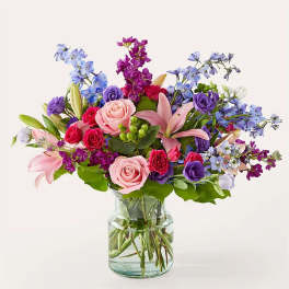 Mixed bouquet of pink, purple, and blue flowers in a glass vase