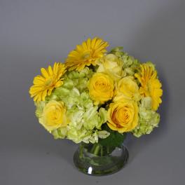 Yellow roses and gerbera daisies in a clear glass vase
