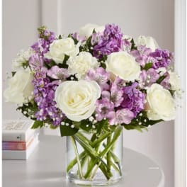 Bouquet of white roses and purple flowers in a clear glass vase
