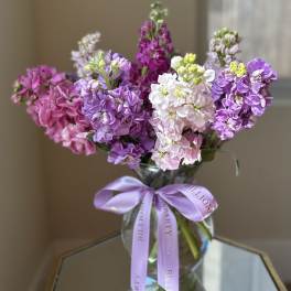 Bouquet of purple, pink, and white flowers in a glass vase with a lavender ribbon