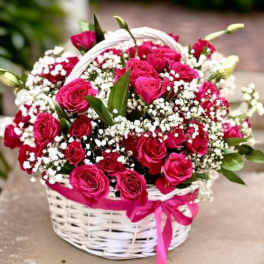 Pink roses and white baby's breath in a white basket with a pink ribbon.