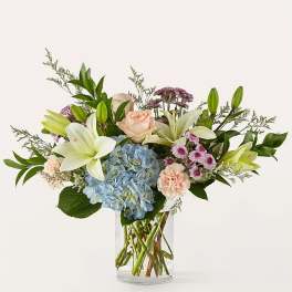 Bouquet of lilies, roses, hydrangea, and carnations in a clear glass vase