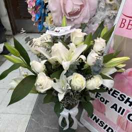 White lilies and roses arranged in a glass vase with a white ribbon