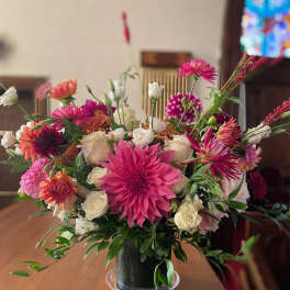 Low glass vase of pink dahlias and white roses with mixed bright blooms on a wooden table