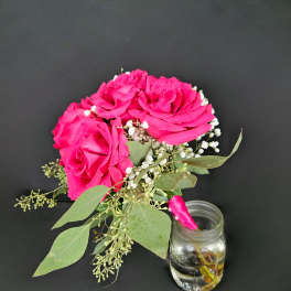 Pink roses with baby's breath and greenery beside a small glass jar