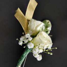 White rose boutonniere with tiny white filler flowers, gold ribbon, and pearl pins on a dark background.