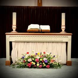Colorful mixed floral spray with roses and other blooms arranged at the base of a church altar table