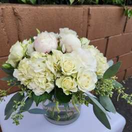 Low round arrangement of white roses, hydrangeas, and peonies in a clear glass vase