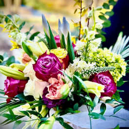 Hand-tied bouquet with bright pink roses, yellow blooms, lilies and mixed flowers wrapped in white paper