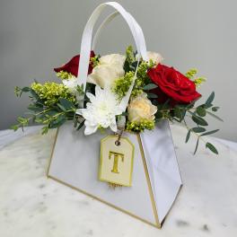 White handled gift bag with red and white roses and a white chrysanthemum