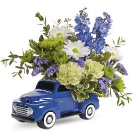 Blue toy truck filled with white, blue, and green flowers