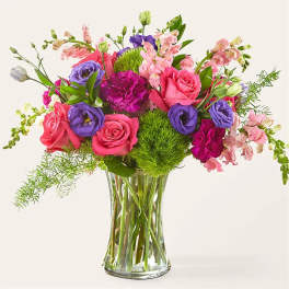 Mixed pink, purple, and white flowers arranged in a clear glass vase