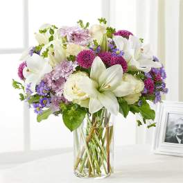 Bouquet of white lilies, cream roses, and purple flowers in a clear glass vase