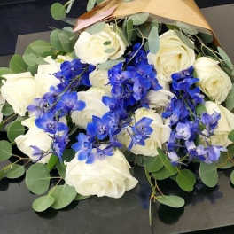 Bouquet of white roses and bright blue orchids wrapped in gold paper