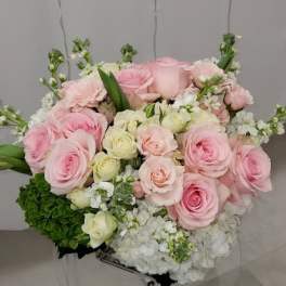 Round arrangement of pink and cream roses with white hydrangeas on a clear stand