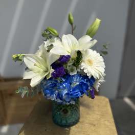 White lilies and blue hydrangeas in a teal glass vase