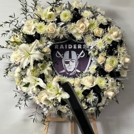 White floral funeral wreath on an easel with a black ribbon