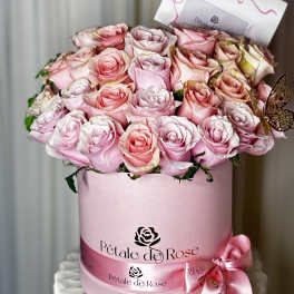 Pink and blush roses arranged in a round pink hat box with a ribbon bow.