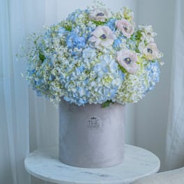 Blue and white floral arrangement in a gray hatbox