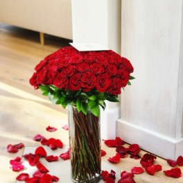 Red roses in a tall glass vase with rose petals scattered around