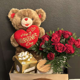 Teddy bear with a Valentine heart beside red roses and gift boxes
