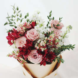 Bouquet of pink roses, red flowers, and white blooms wrapped in gold paper