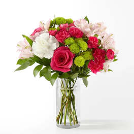 Bright pink roses and carnations with green button mums and white blooms in a clear glass vase.