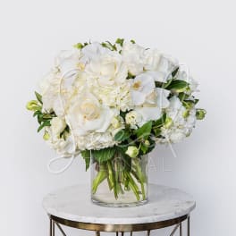 White roses and orchids arranged in a clear glass vase