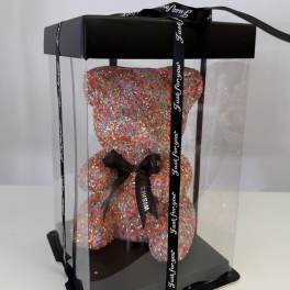 Multicolored teddy bear in a clear gift box with black ribbon