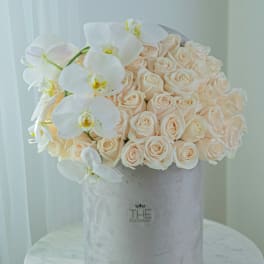 Cream roses and white orchids arranged in a gray hat box