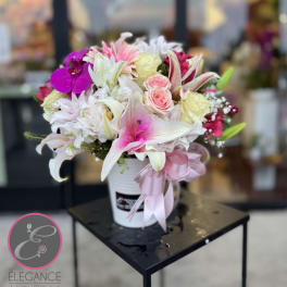 Pink and white floral arrangement in a white bucket with a pink ribbon