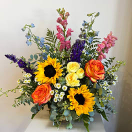 Colorful mixed bouquet with sunflowers, roses, and tall blue and pink blooms in a vase