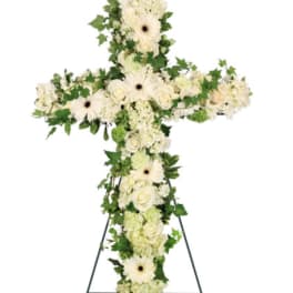 White floral cross on a stand with green foliage