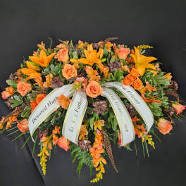 Orange lilies and roses casket spray with white sympathy ribbons on a dark background