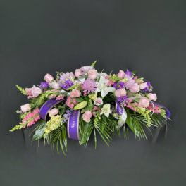 Pink and purple floral casket spray with white lilies and ribbon