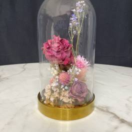 Dried pink and purple flowers under a glass dome on a gold base