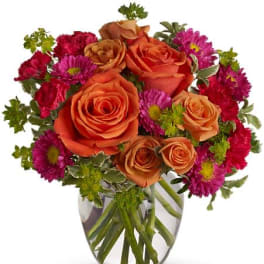 Orange roses and magenta daisies in a clear glass vase