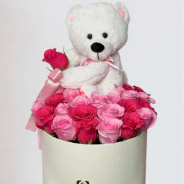 White teddy bear sitting in a box of pink roses with a ribbon