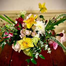 Mixed bouquet with yellow daffodils, pink roses, and white blooms in a round vase on a wooden table