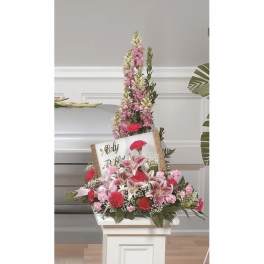 Tall floral standing arrangement with a memorial sign and pink lilies