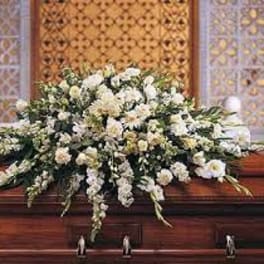 Large white floral casket spray on a wooden casket