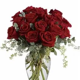 Red roses arranged in a clear glass vase with trailing greenery