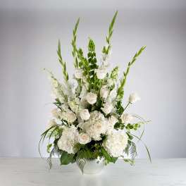 Tall white arrangement of roses, hydrangeas, and green Bells of Ireland in a white bowl vase