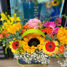 Bright mixed bouquet with sunflowers, gerbera daisies, and orange roses in a handled basket