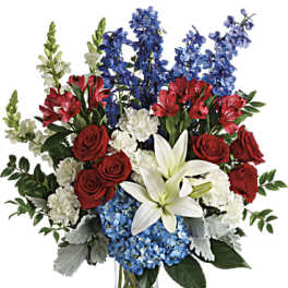Red roses, white lilies, and blue flowers in a clear glass vase